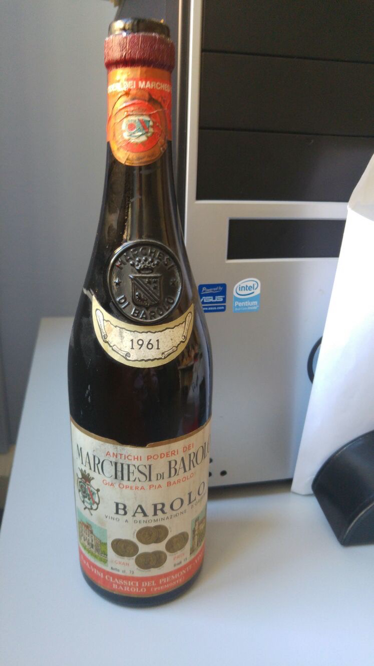 La foto mostra una bottiglia di vino posizionata su un tavolo, La bottiglia è etichettata come  marchesi di barolo, barolo, con l'indicazione dell'anno 1961, sull'etichetta sono presenti anche medaglie e riconoscimenti, il tappo della bottiglia è sigillato ceralacca rossa su cui impresso lo stemma dei barolo